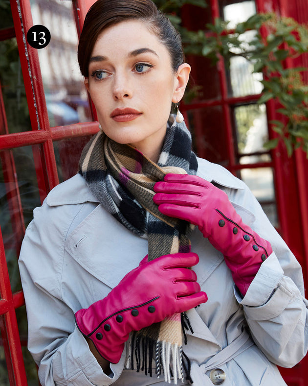 Woman wearing leather gloves with pipping and buttons in fuchsia with cashmere scarf leaning on a red telephone box