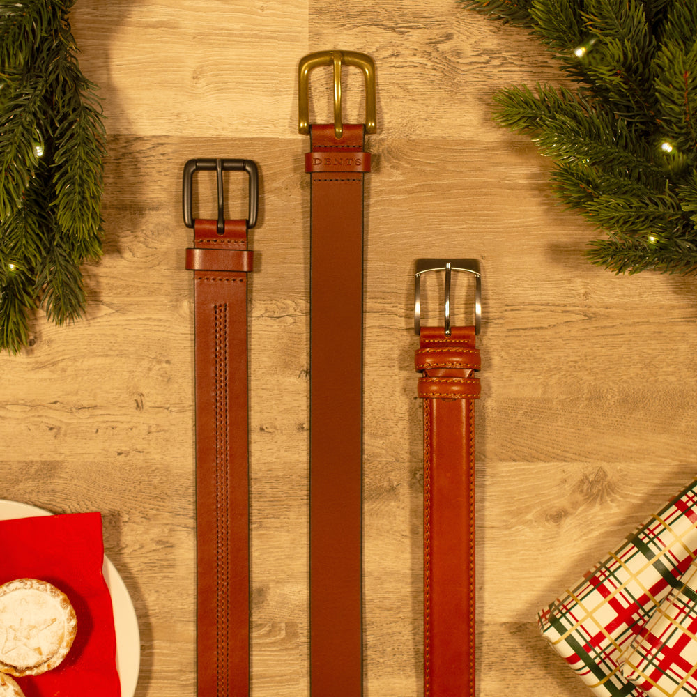 Selection of men's brown leather belts against a wooden background with Christmas accessories