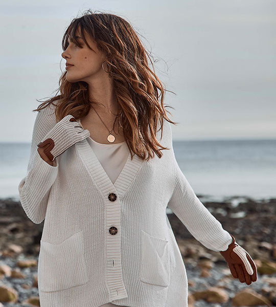 Woman wearing crochet back leather gloves in white and brown on a beach.
