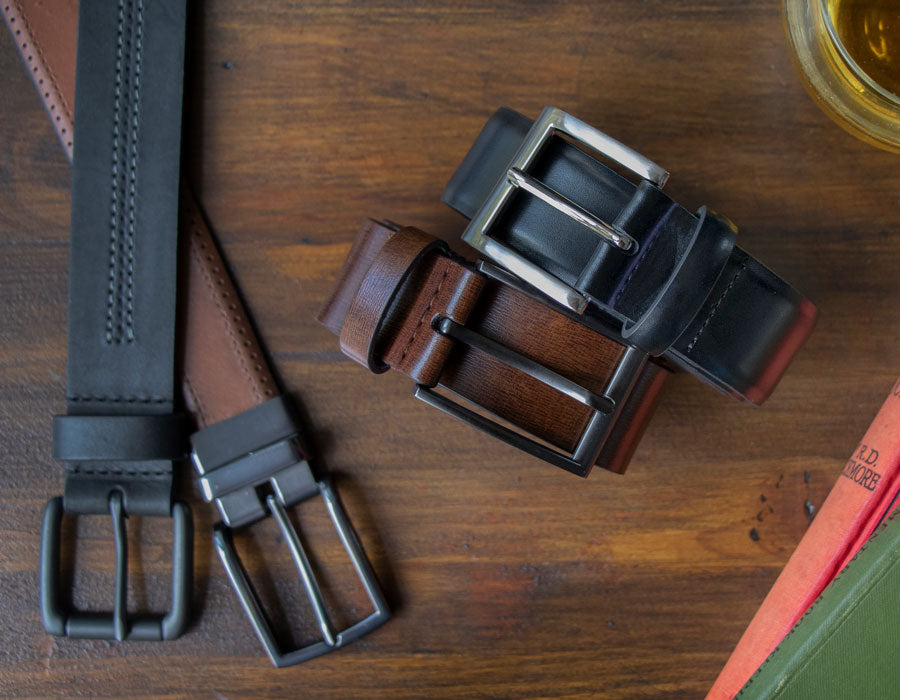 Men's leather belts in various styles and colours laid out on a table