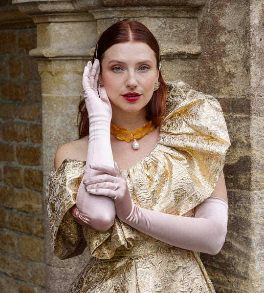 Woman wearing long evening satin gloves in rose with a gold dress outdoors
