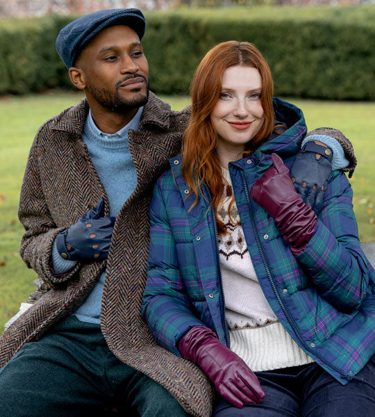 Man and woman sitting on a bench outdoors wearing leather gloves and tweed hat