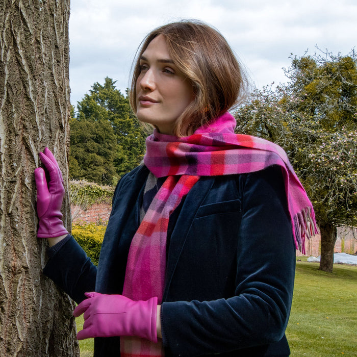 Woman wearing heritage plaid check cashmere scarf with tassels in cherry with a velvet jacket and leather hot pink gloves