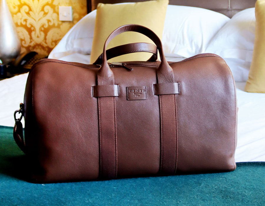 Men's leather weekender bag laid out on a hotel bed
