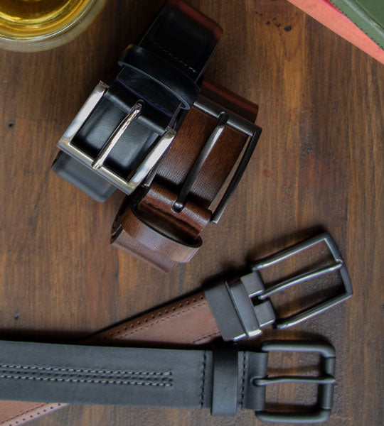Men's leather belts in various colours and styles laid out on a wooden table