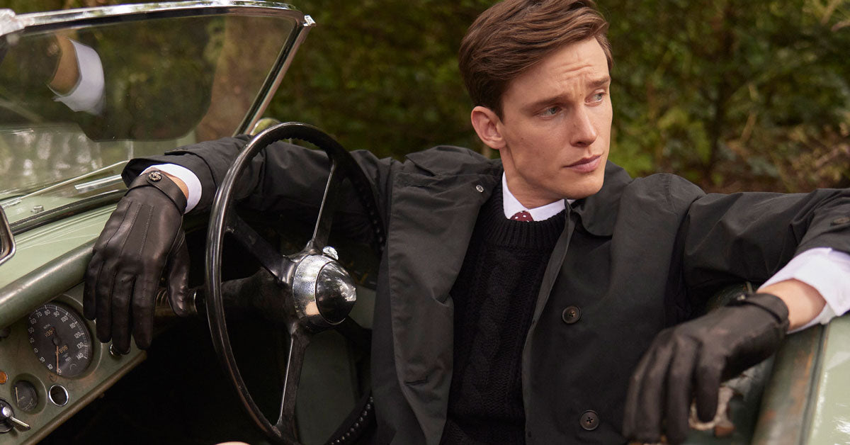 man wearing leather driving gloves in black sitting in a classic car
