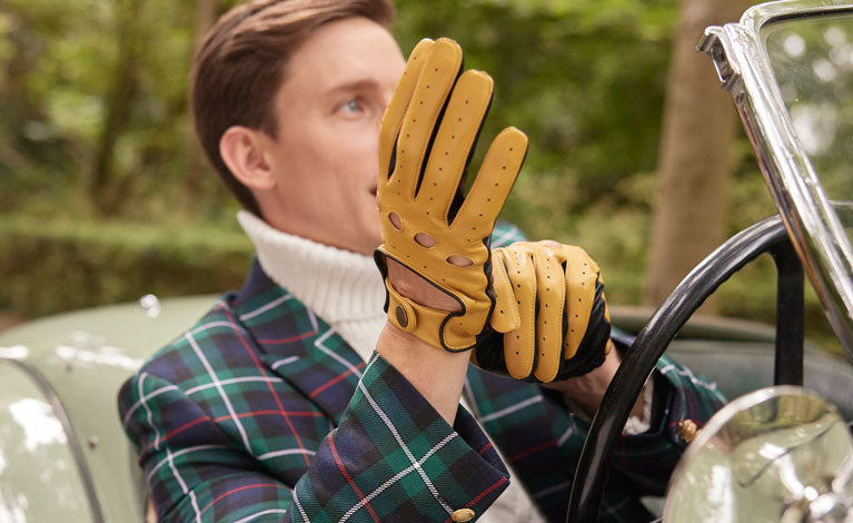 Man wearing leather driving gloves in cork/black behind the wheel of a classic car