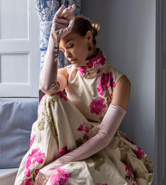 Woman wearing long satin gloves with button in rose sitting by the window