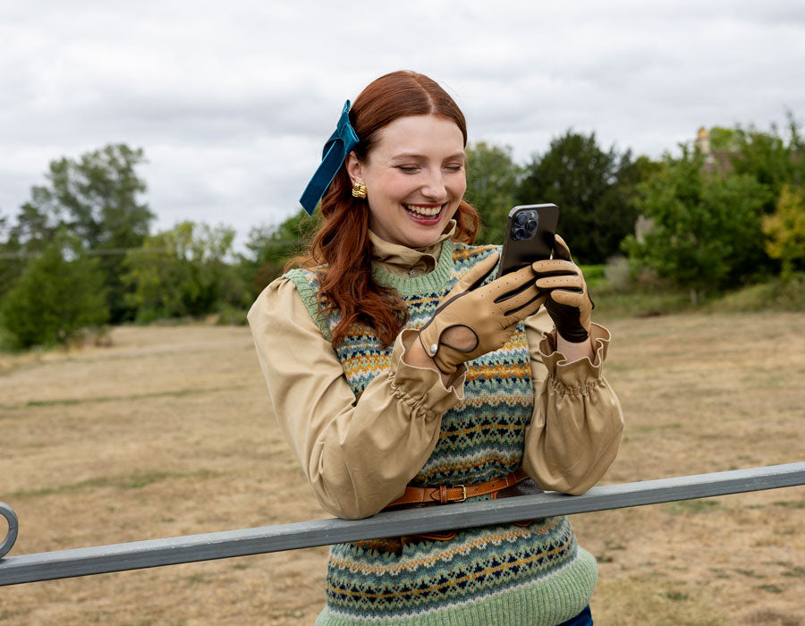 Woman wearing touchscreen leather driving gloves in toffee using her mobile phone