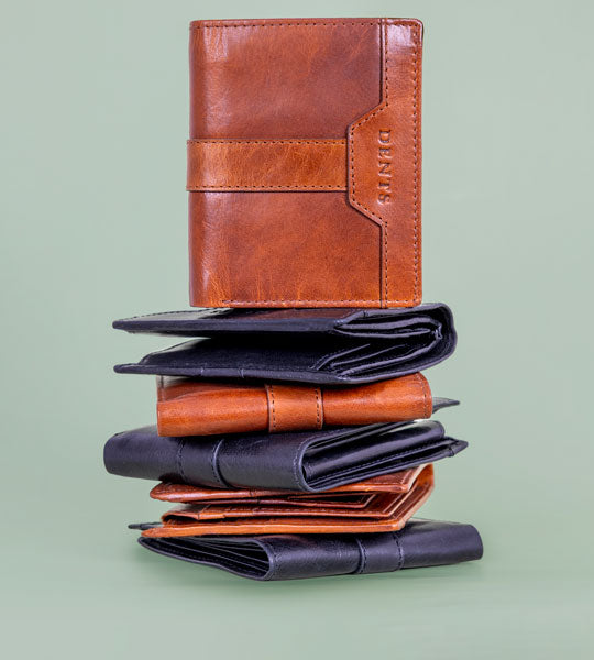 Men's leather wallets in various colours and styles stacked on top of each other on a green background