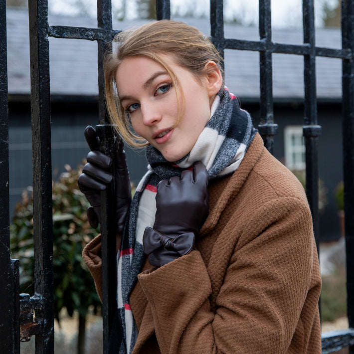 Woman wearing leather gloves with a bow and a check scarf by a metal gate