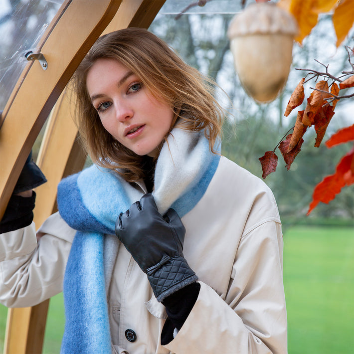 Woman wearing grey leather gloves and a blue blanket scarf