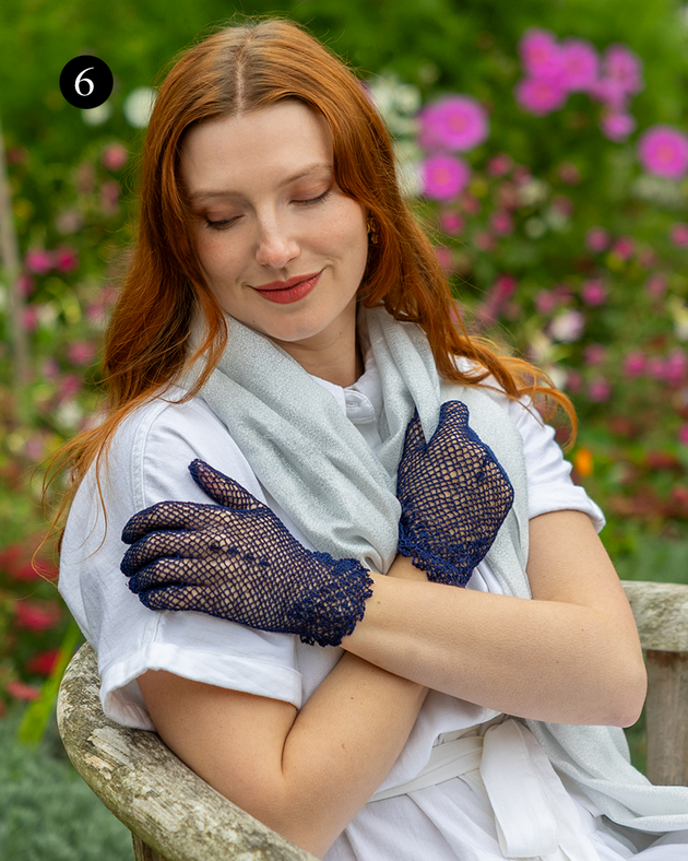 Woman wearing cotton crochet gloves in navy, arms crossed in the garden.