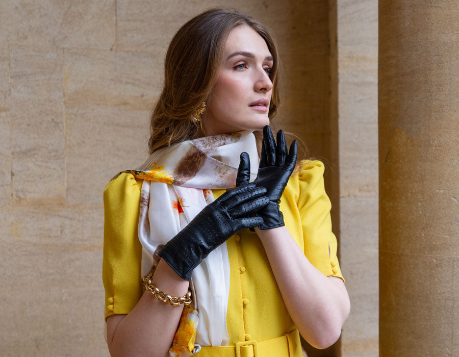 Woman wearing luxury leather gloves in navy, outside in yellow dress.