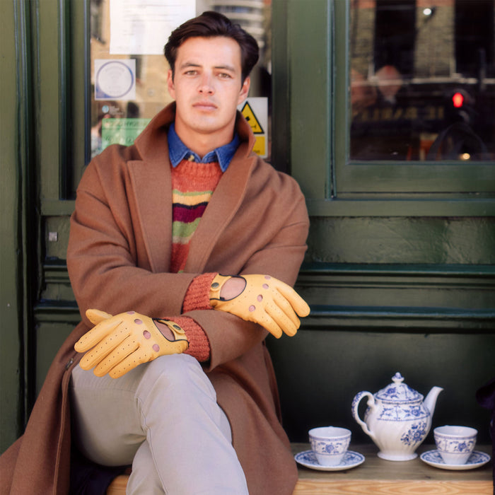 Man wearing cork yellow and black driving gloves sat outside a cafe